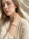 Woman wearing a pearl bracelet against a soft, neutral background