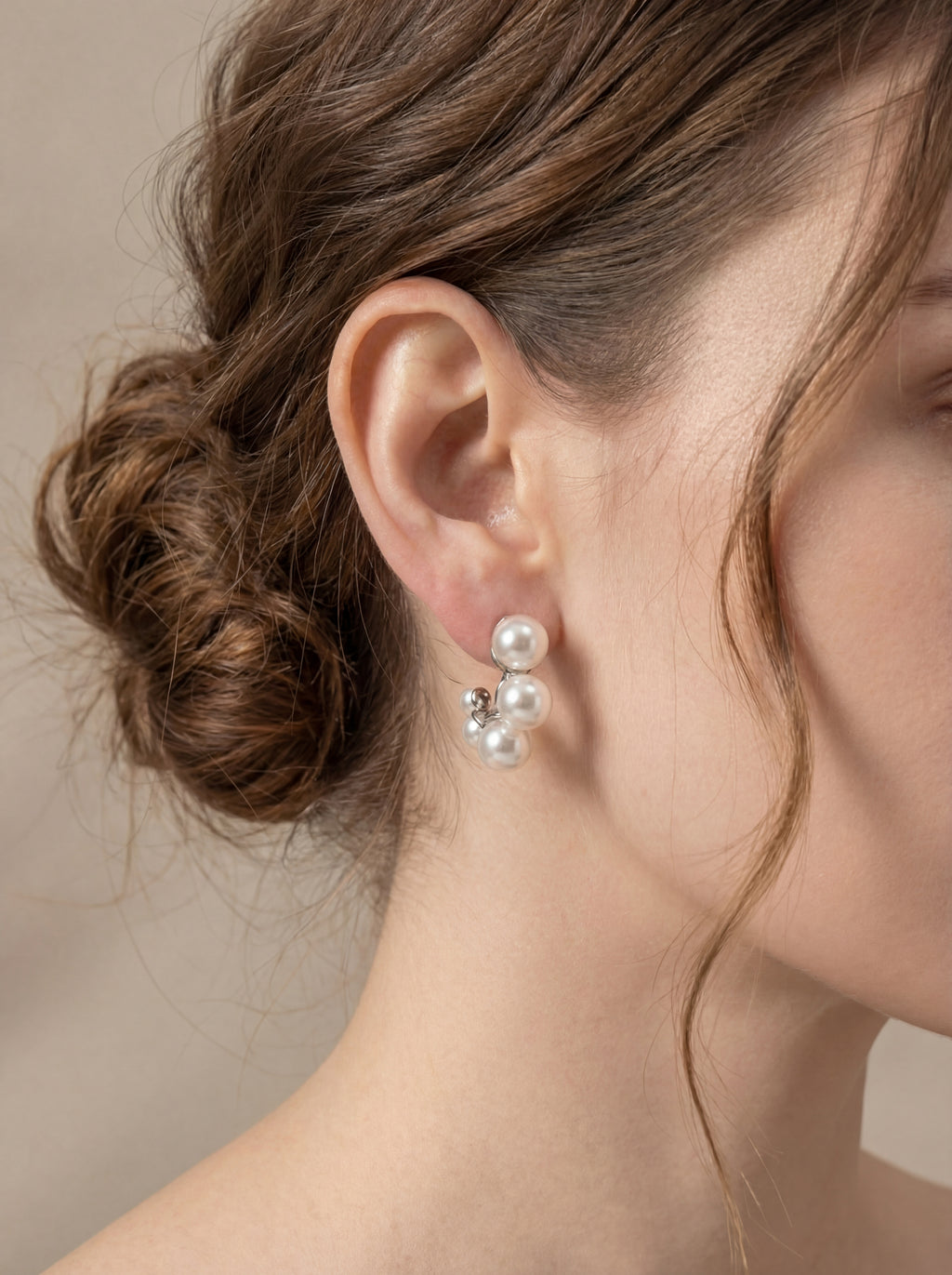 Close-up of a person wearing pearl earrings with a neutral background